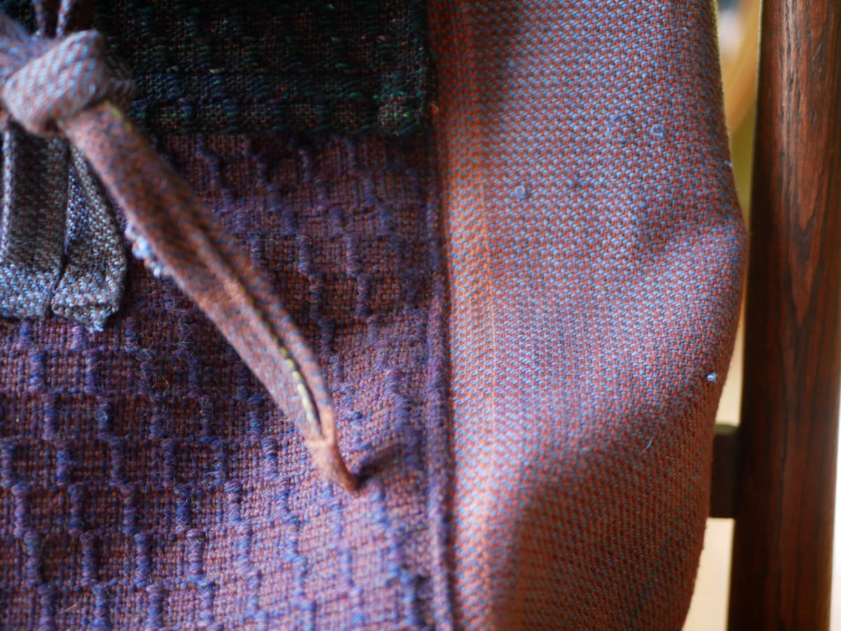 close-up of the bag. purple bumps ripple across the front. ribbons tie onto a fabric loop.