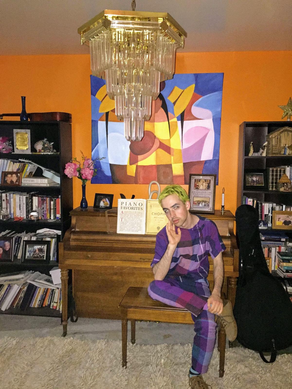 rosemary seated on a piano bench in someone else's living room, with short green hair, wearing this full-body purple outfit