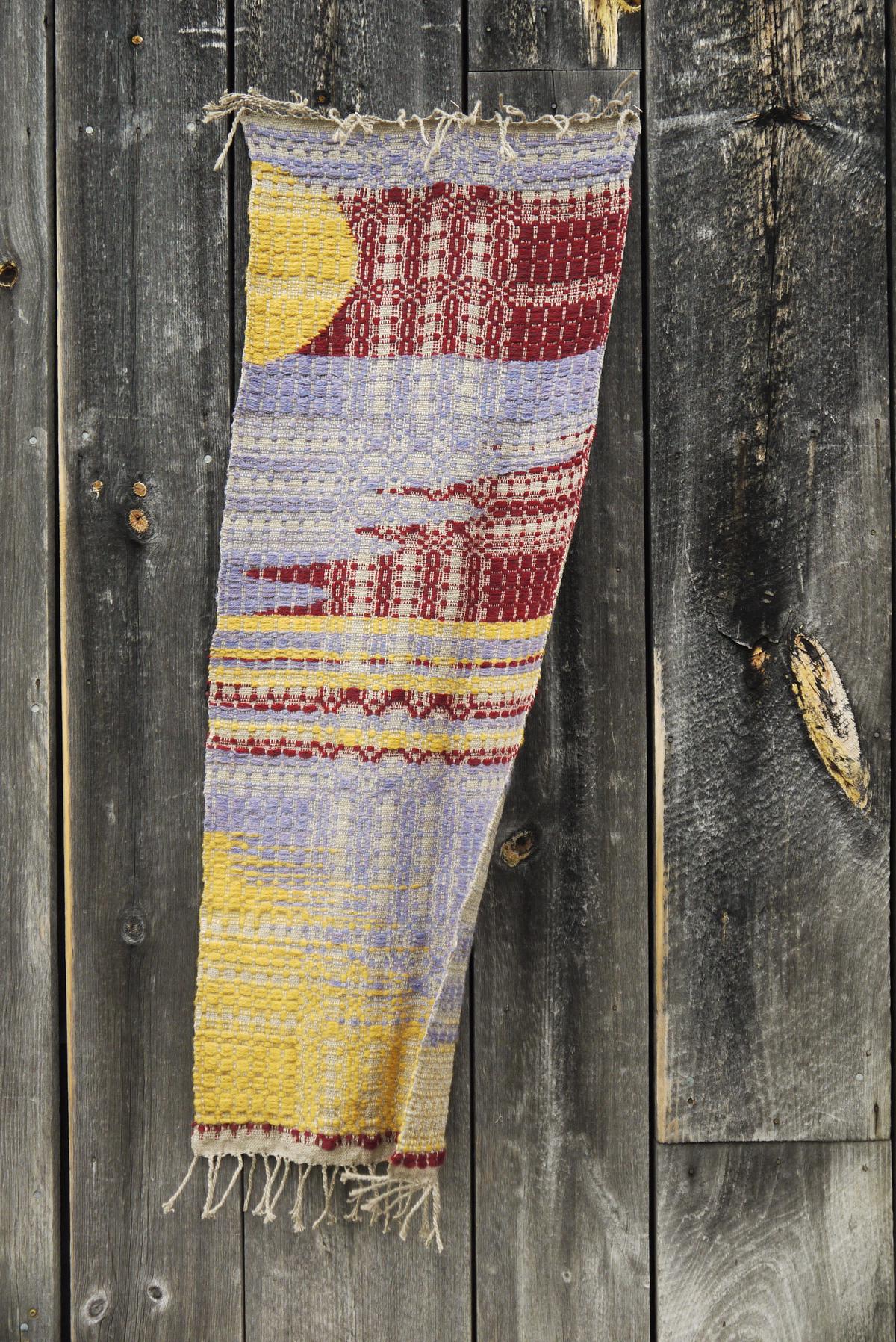 long table runner hanging vertically on the darkened wood wall outside a barn