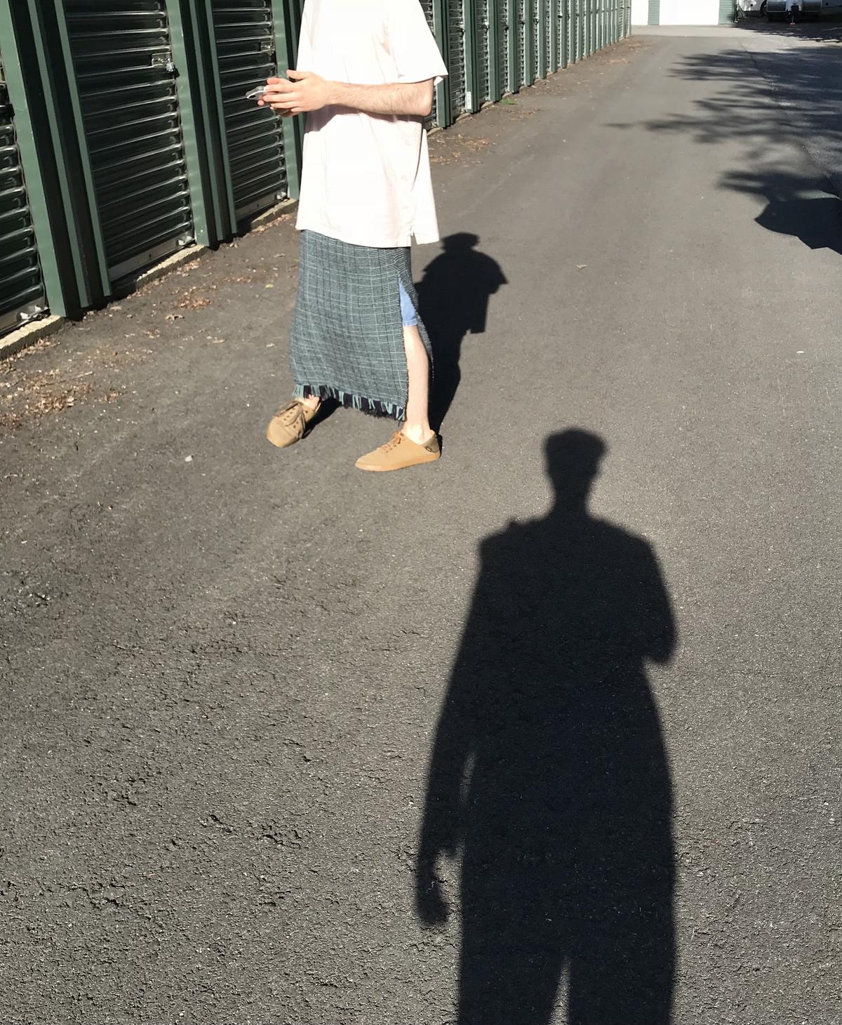 a cropped shot of the skirt being worn in front of a line of storage lockers. a side slit reveals a leg. the photographer's shadow is long on the pavement.