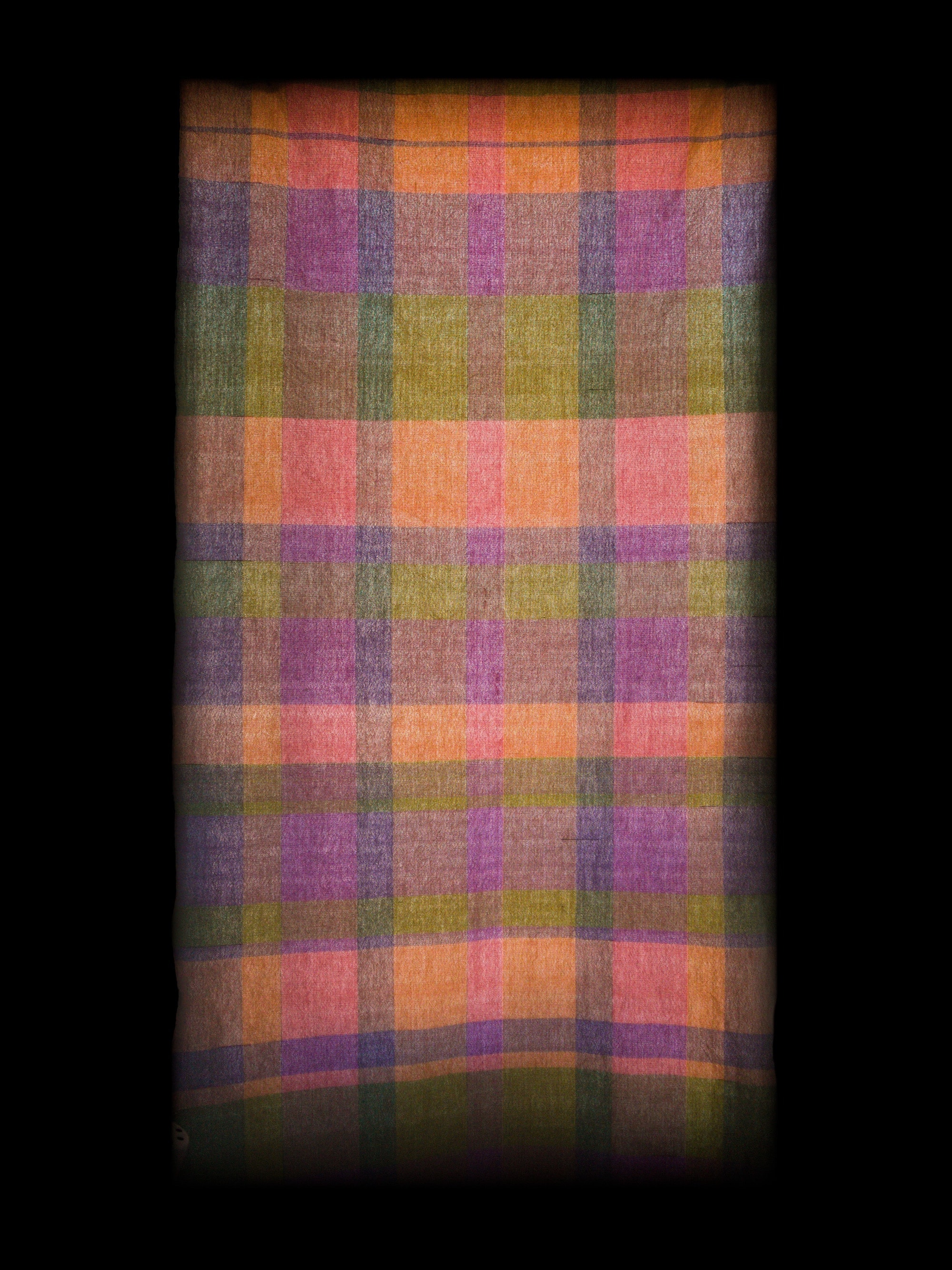 a backlit rectangle of cloth, with long interlocking stripes in earthy green, orange, purple, and pink. it's abstract, but its glow feels heightened or reverential. the edges fade into a black background.