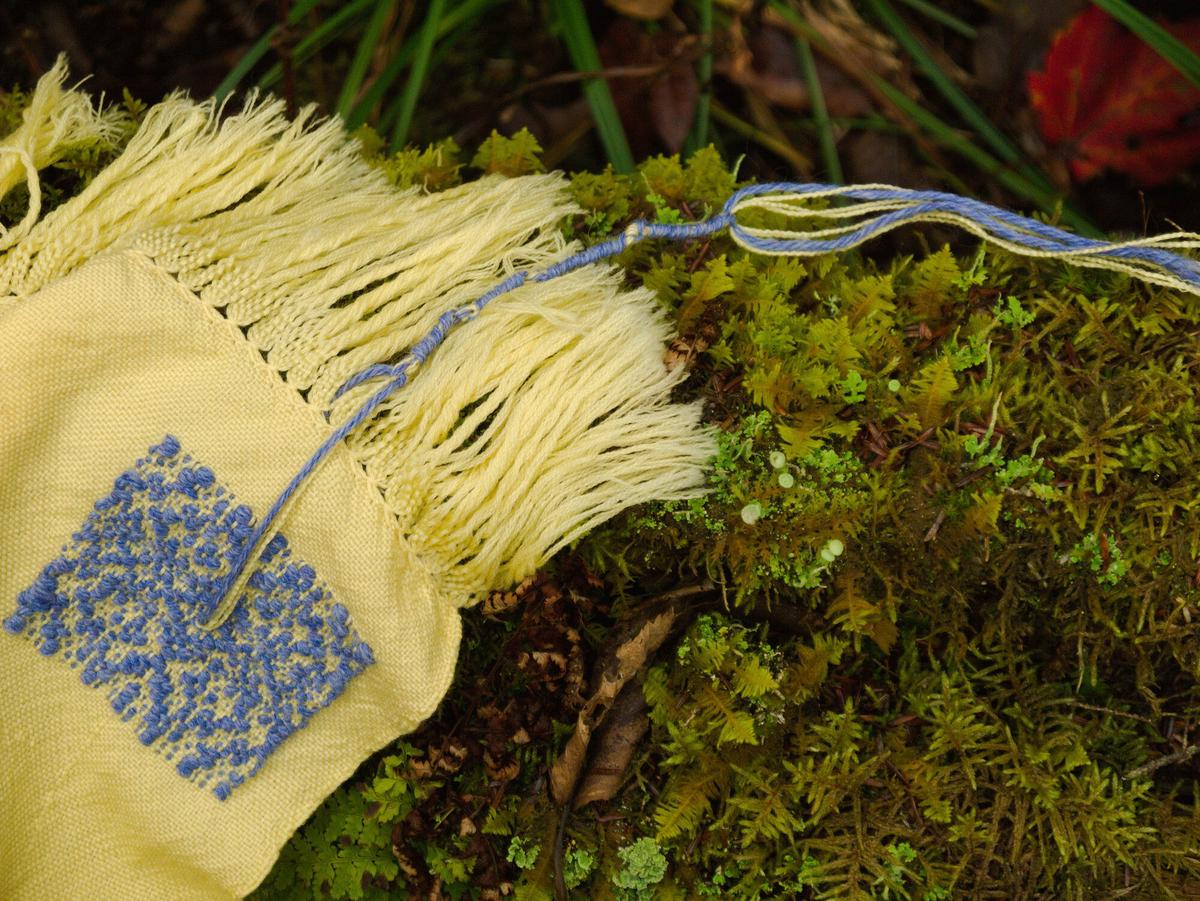 a corner of the tallis decorated with a square of blue crystaline inlay and tzitzit. resting on a patch of moss.