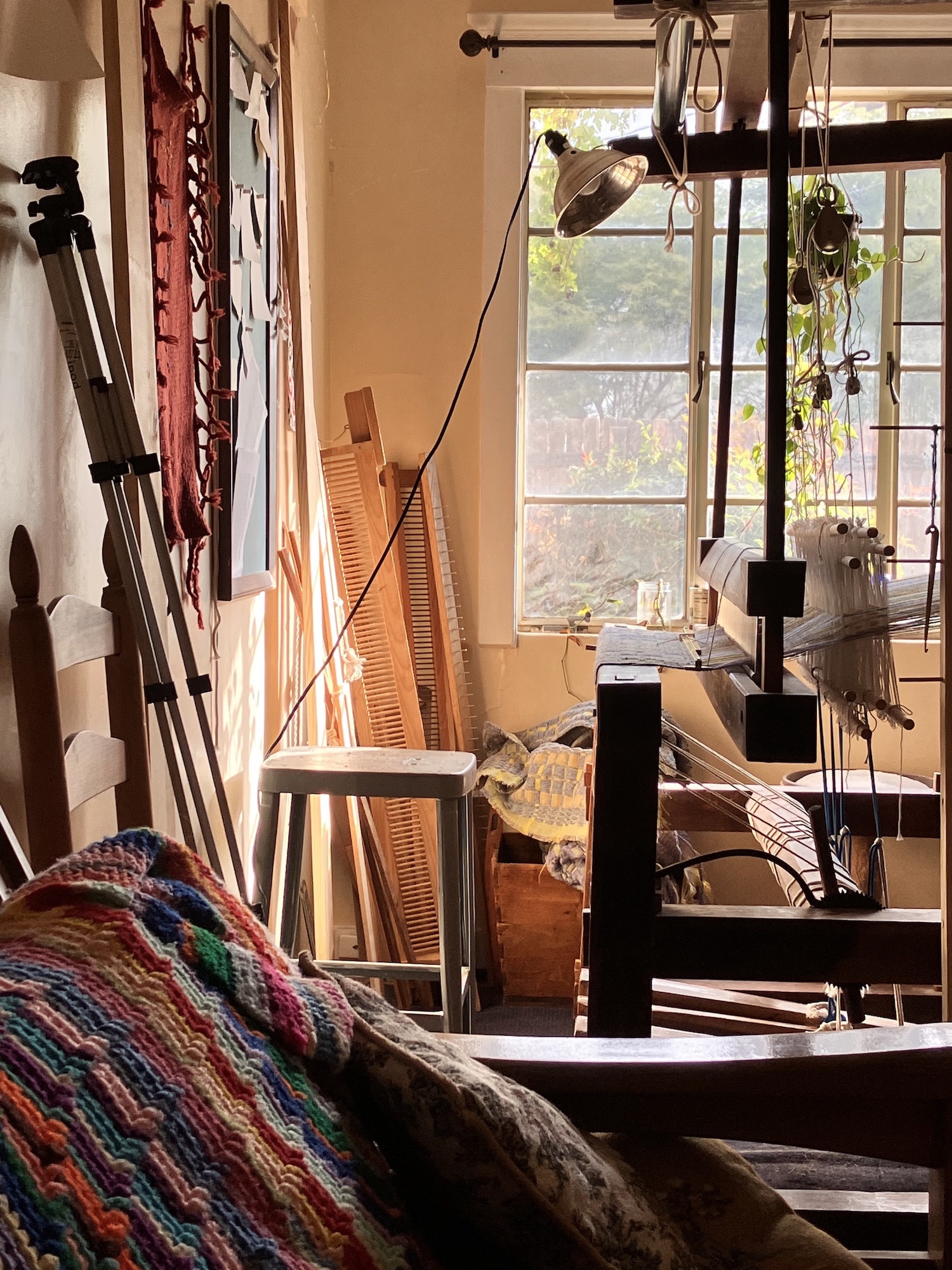 the loom corner of my studio in the bright morning light. bright textiles and wooden sticks everywhere.
